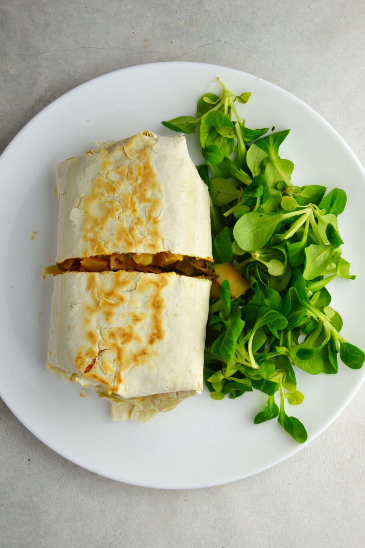 Tortilla z mozzarellą i kapustą w pomidorach przecięta w połowie na białym talerzu